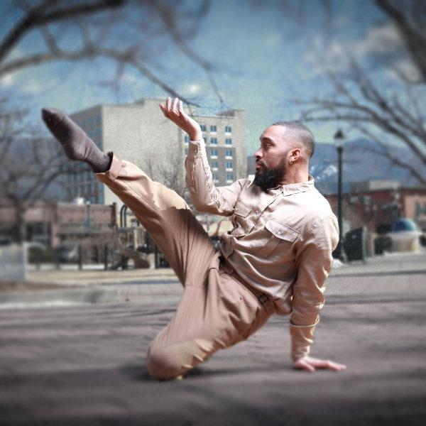 A dancer balances on one knee with one hand on the ground while extending the other leg and arm.