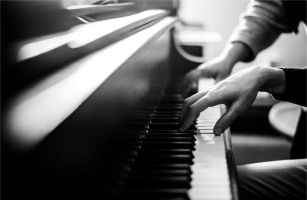 A closeup of piano keys shows one h和 from each of two people playing the keys.