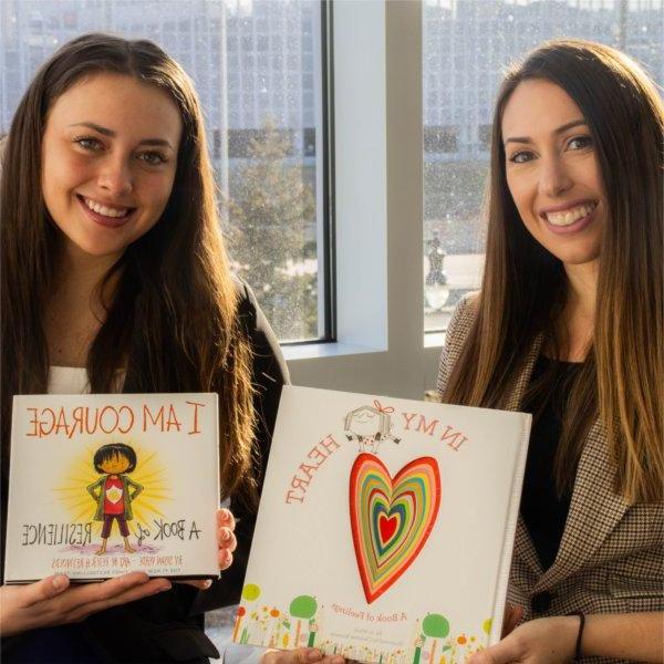 two women seated next to each other holding children's books