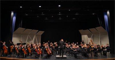 concert band on stage with conductor in center, all musicians in black