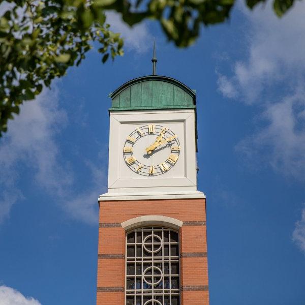 The top of the carillon tower is set against blue sky 和 wispy clouds with some green tree leaves in the foreground.